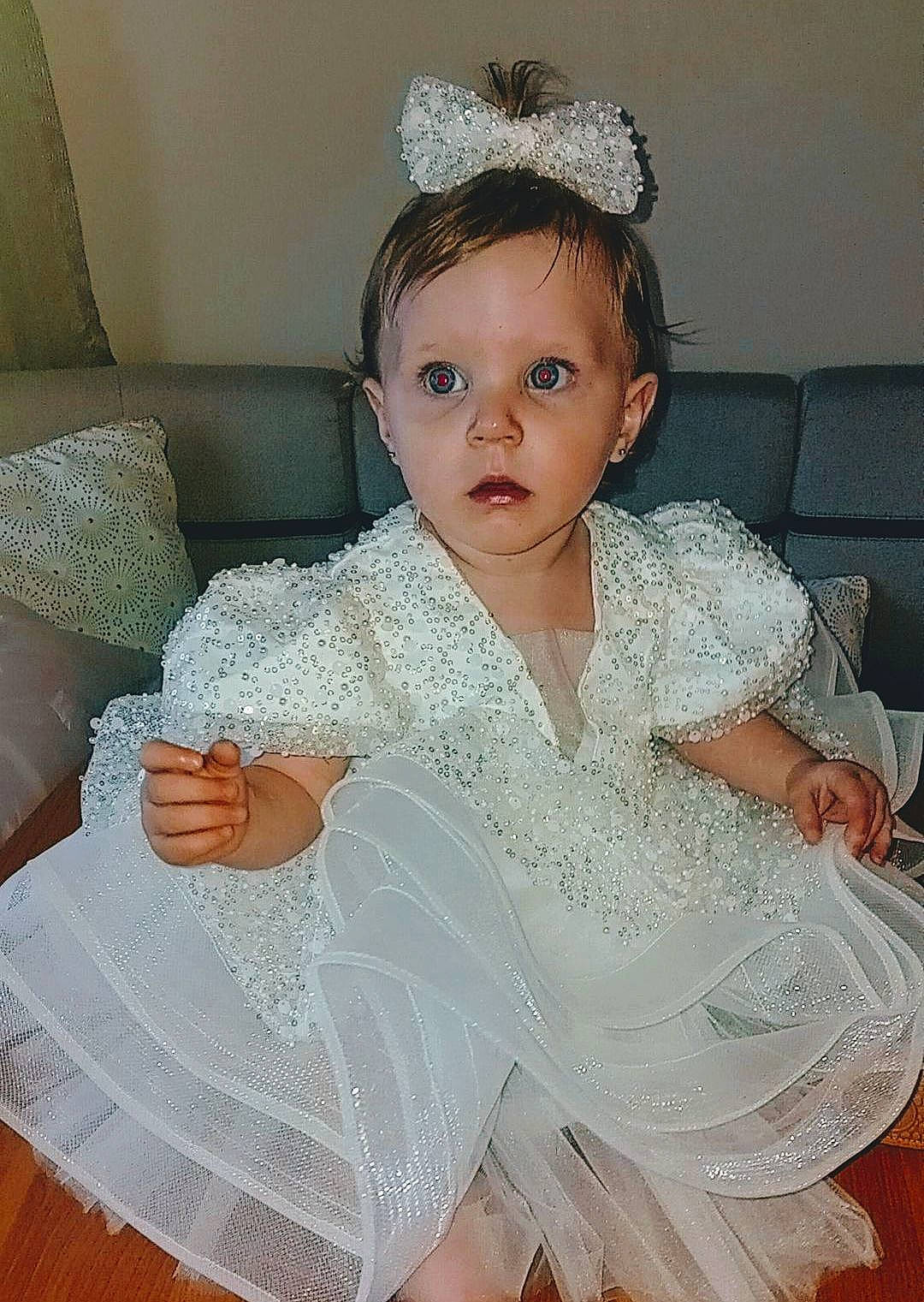 Talya participe au concours pour gagner de l'argent avec cette photo : baby_toddler_clothing, bridal_accessory, child, day_dress, dress, embellishment, event, eyelash, fashion_design, headband, headpiece, iris, jewellery, necklace, person, pink, sitting, skin, surprise, textile
