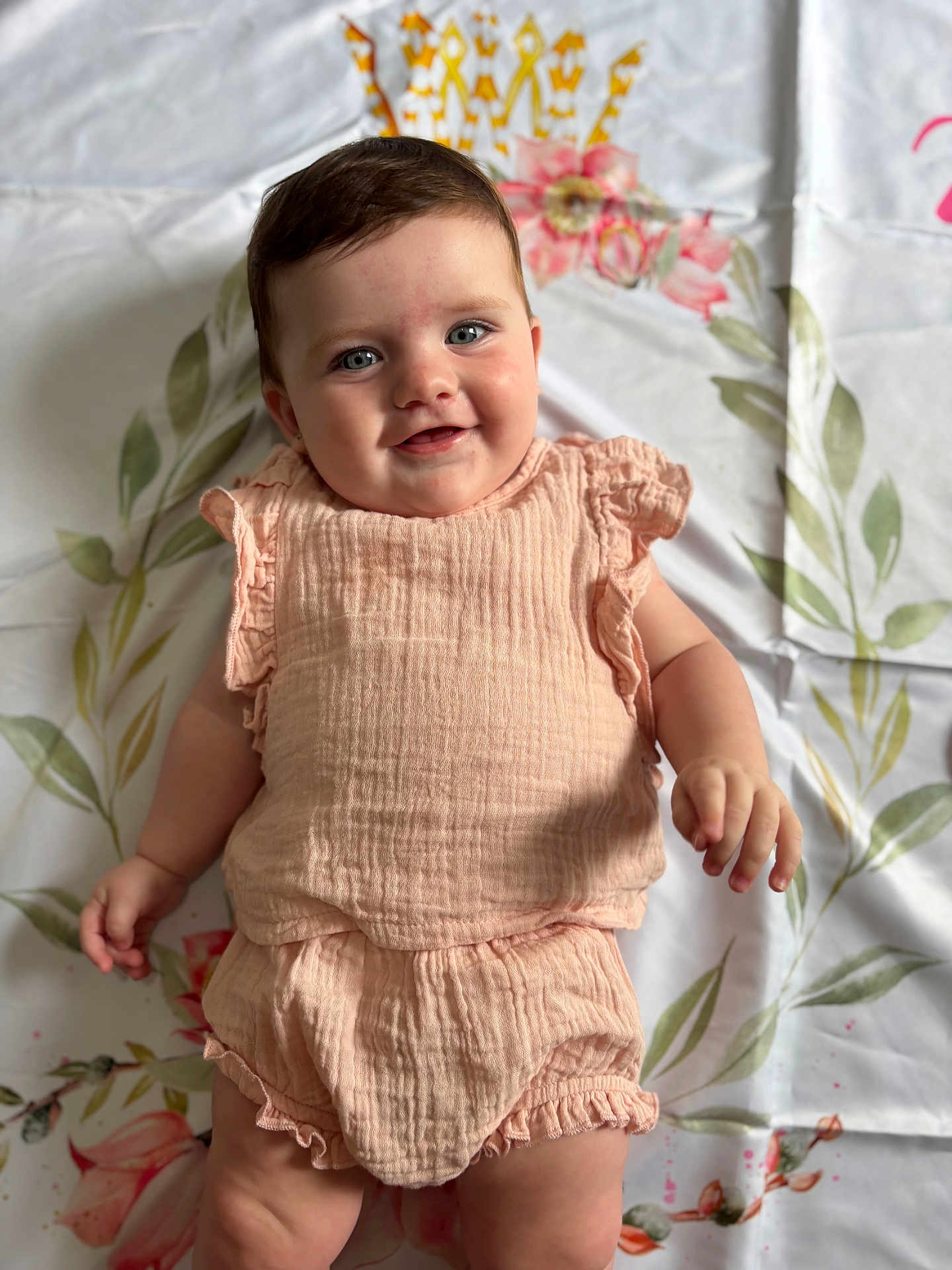 Arabella is registered to the contest to win money with this photo: baby, infant, smiling, blue_eyes, peach_outfit, ruffles, floral_blanket, cute, chubby, portrait, lying_down, happy, child, soft_lighting, indoor, person, skin, face, hand, young