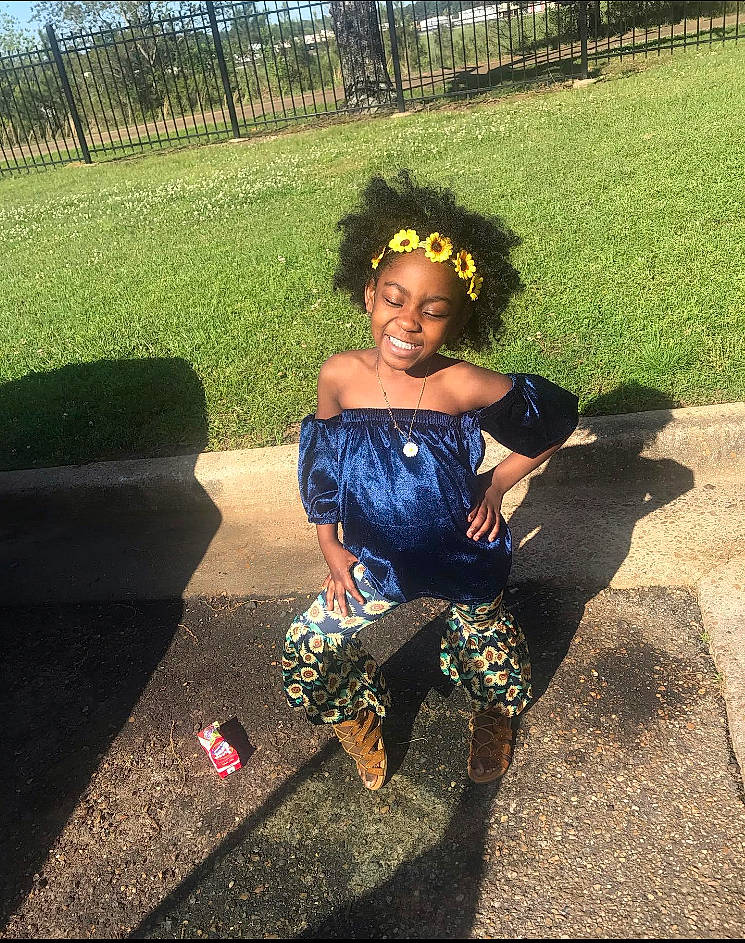 Mylee is registered to the contest to win money with this photo: black_hair, cool, dress, footwear, grass, hair, hairstyle, joint, joy, leg, long_hair, person, plant, recreation, shoe, shoulder, sitting, smile, summer, toddler