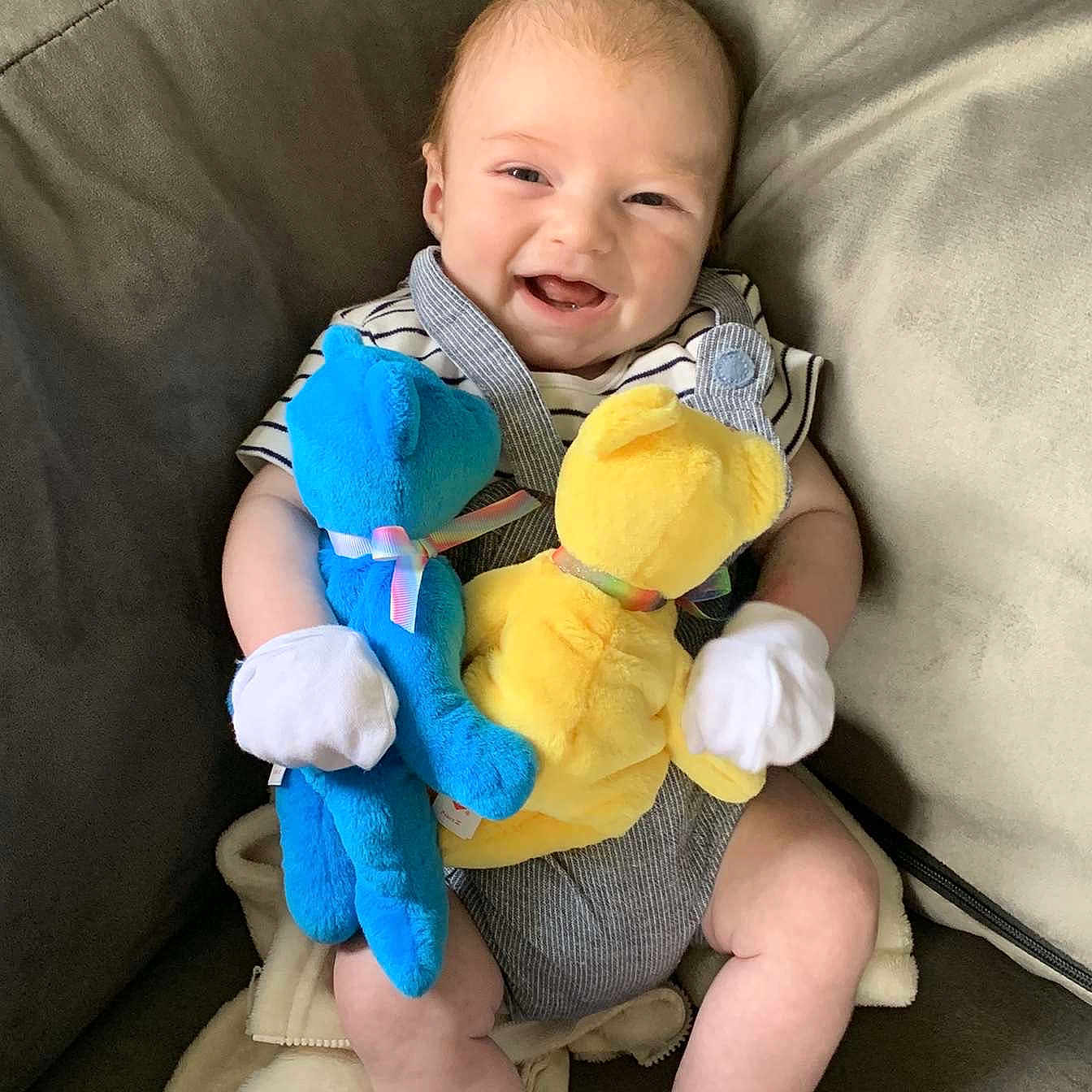 Theo is registered to the contest to win money with this photo: baby, blanket, blue, child, clothing, couch, cute, face, happy, indoor, infant, mittens, person, plush_bear, seated, smiling, socks, striped, toy, yellow