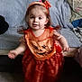 toddler, child, orange_dress, pumpkin_face, headband, barefoot, carpet, couch, blanket, indoor, motion_blur, smiling, cute, baby, person, home, wall_photos, furniture, fabric, playful
