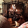 cat, pet, animal, indoors, fireplace, fire, hearth, stone_wall, warm_lighting, cozy, blanket, chair, furniture, wood, decorative_screen, deer_silhouette, rustic, home, portrait, relaxed