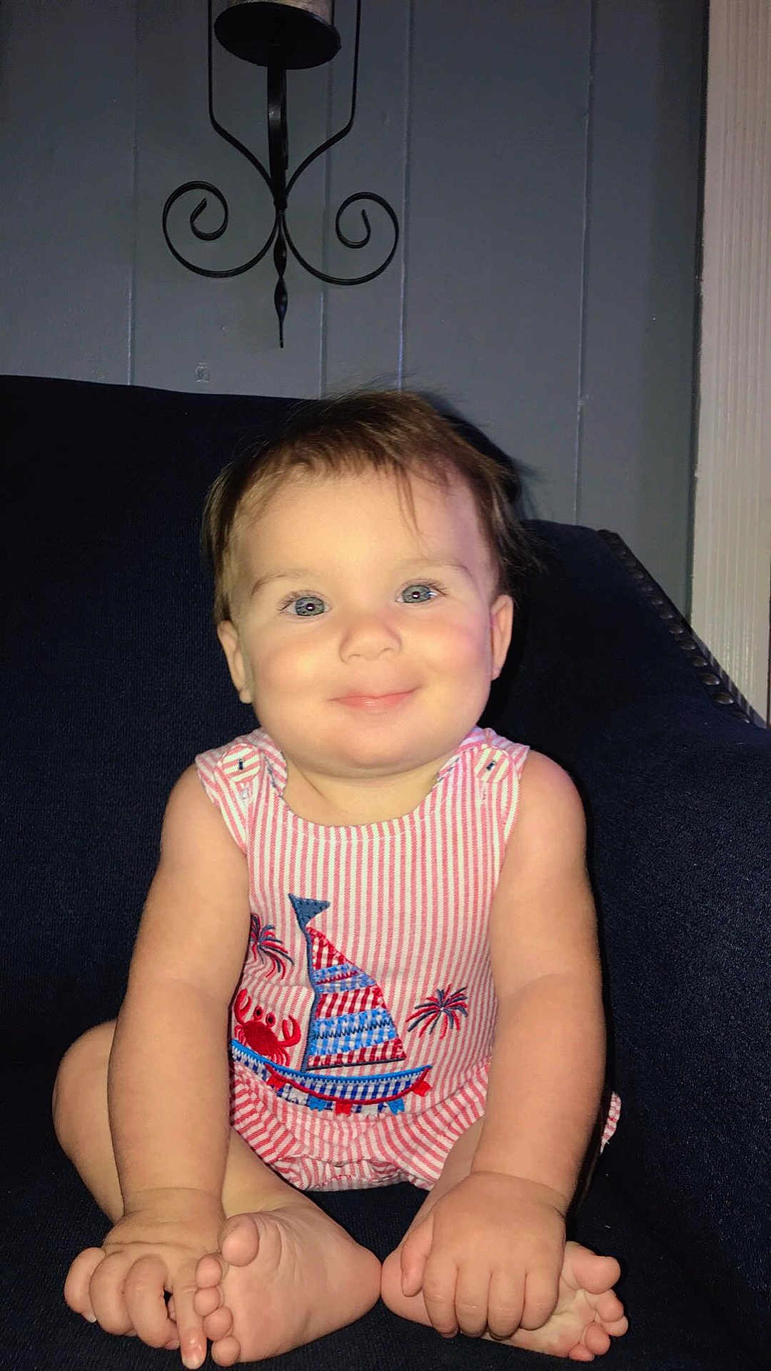 Callum is registered to the contest to win money with this photo: baby, child, smiling, blue_eyes, striped_clothing, romper, sailboat, crab, sitting, barefoot, couch, indoor, wall_sconce, cute, happy, chubby_cheeks, hands, feet, portrait, person