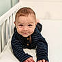 baby, crib, toddler, smiling, face, hands, striped_clothing, wooden_buttons, indoor, white_crib, cute, child, infant, lying_down, portrait, curious, happy, soft_light, closeup, person