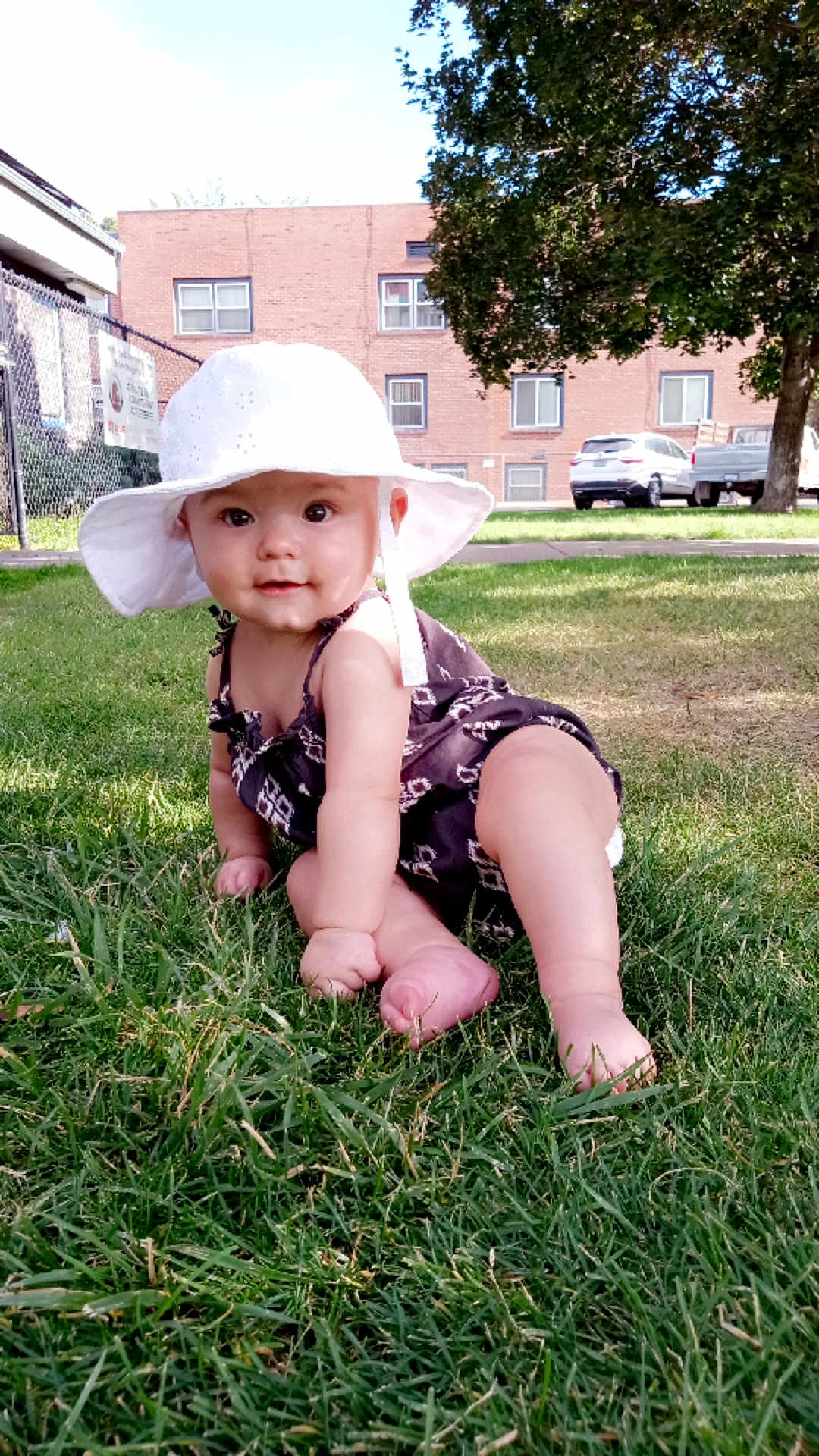 Theryn joined the competition — help win amazing prizes! baby, hat, grass, outdoor, sunlight, child, greenery, building, tree, car, sidewalk, smile, curious, summer, nature, infant, candid, cute, portrait, playful