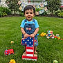 toddler, child, birthday, grass, toy, number_one, overalls, blue_shirt, smiling, outdoor, happy, play, duck_toy, fire_truck_toy, teddy_bear, blocks, banner, garden, greenery, celebration