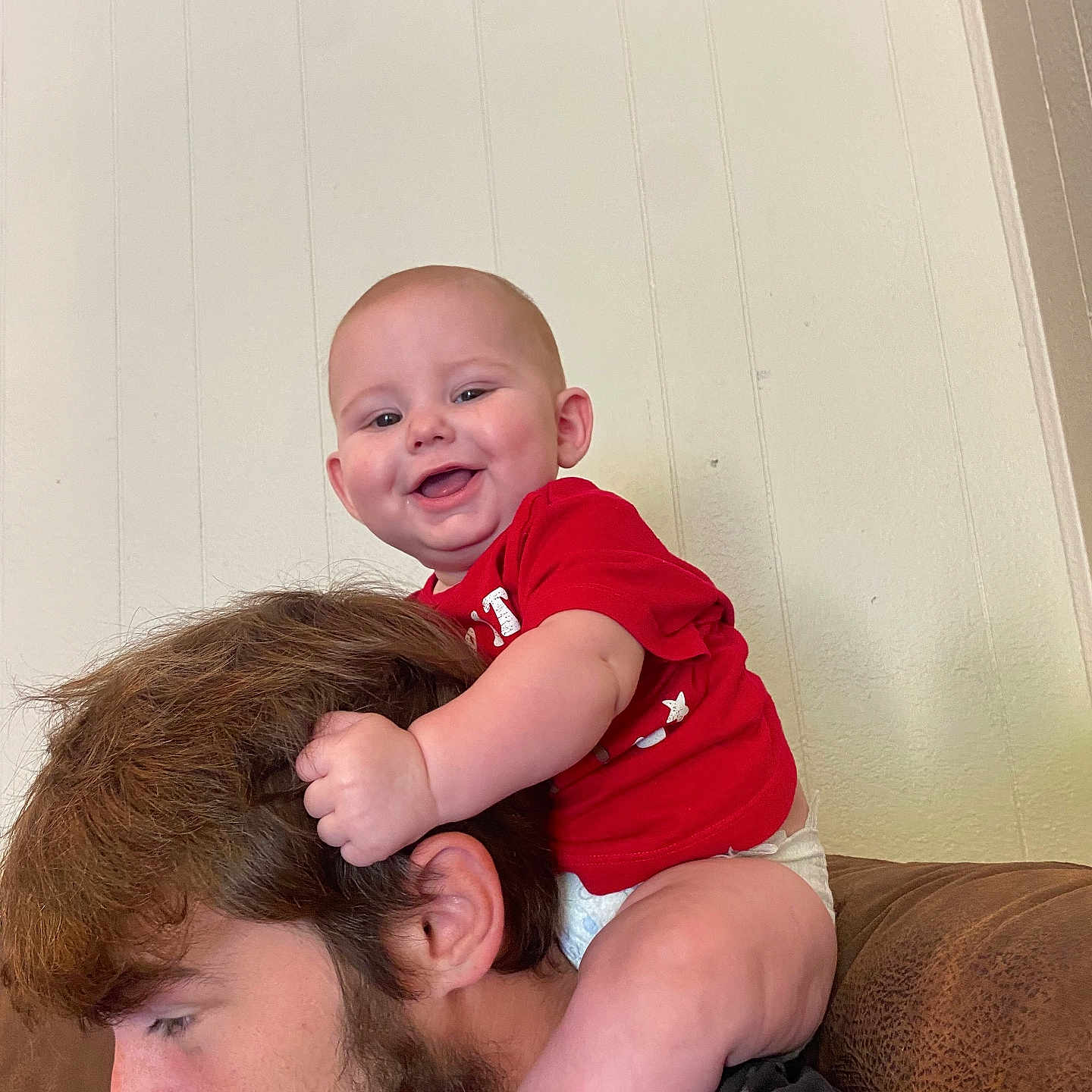 Brodie is registered to the contest to win money with this photo: baby, beard, casual, child, couch, diaper, face, family, hair, happy, head, holding, indoor, man, person, red_shirt, shoulders, skin, smile, wall
