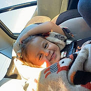 Clementine joined the competition — help win amazing prizes! child, toddler, smiling, happy, portrait, car, car_seat, vehicle, blanket, wrapped_up, winter_clothing, sunlight, indoor, travel, face, head, brown_hair, seated, daylight, photography
