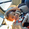 child, toddler, smiling, happy, portrait, car, car_seat, vehicle, blanket, wrapped_up, winter_clothing, sunlight, indoor, travel, face, head, brown_hair, seated, daylight, photography