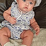 Bonnie is registered to the contest to win money with this photo: baby, infant, child, blue_eyes, white_hat, floral_romper, sitting, knitted_blanket, couch, curious, sock, cute, chubby_arms, indoor, portrait, headwear, soft_lighting, young_child, close_up, baby_fashion