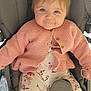 baby, blue_eyes, child, clothing, comfort, cute, cute_expression, face, floral_pants, happy, indoor, infant, knitted, pacifier, person, pink_cardigan, seated, smiling, soft_lighting, stroller