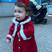 Edena participe au concours pour gagner de l'argent avec cette photo : toddler, child, red_coat, bow, outdoor, stroller, pavement, window, building, smile, curly_hair, earrings, winter_clothing, buttoned_coat, black_pants, person, side_view, daylight, cute, happy