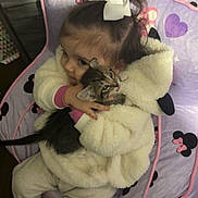 Paisley is registered to the contest to win money with this photo: toddler, child, kitten, cat, hug, bow, hair_accessory, bean_bag, minnie_mouse, purple, pink, jacket, hoodie, pants, shoes, wood_floor, indoor, cute, cozy, pet