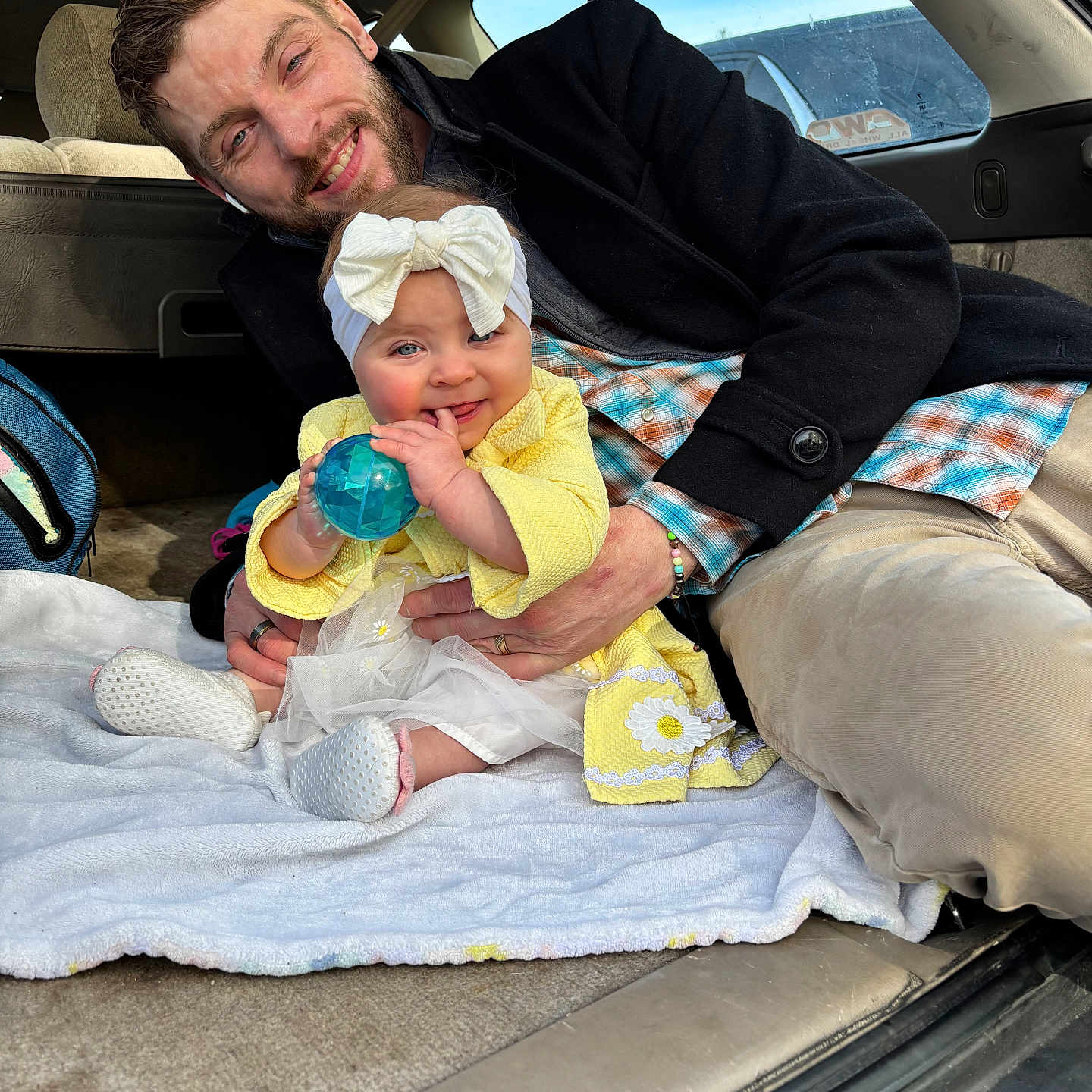 Embyr is registered to the contest to win money with this photo: baby, child, man, smile, toy, car_interior, blanket, yellow_clothing, headband, bow, sitting, happy, family, casual_clothing, plaid_shirt, beard, window, seat, playful, toddler