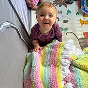 Embyr joined the competition — help win amazing prizes! baby, smiling, blanket, colorful, playmat, toy, doll, indoor, child, happy, infant, purple_clothing, curly_hair, soft_texture, fringe, sitting, looking_up, face, cute, play_area