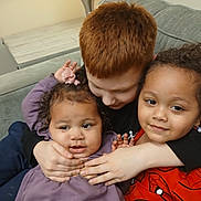 Katalina is registered to the contest to win money with this photo: child, children, couch, hug, affection, purple_clothing, red_hair, curly_hair, smile, indoor, casual, playful, sitting, person, family, toddler, boy, girl, candid, spiderman_shirt