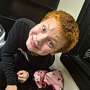 Joshua Jr is registered to the contest to win money with this photo: child, red_hair, smile, black_shirt, sneakers, red_sneakers, pink_blanket, hearts, indoor, mirror, furniture, playful, portrait, person, young, happy, face, clothing, room, hand