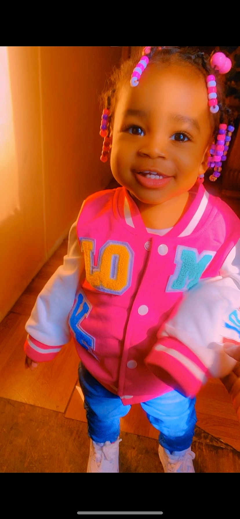 Melaysia joined the competition — help win amazing prizes! child, toddler, smiling, braids, beads, pink_jacket, colorful_clothing, jeans, white_sneakers, indoor, wooden_floor, happy, portrait, cute, standing, person, young_child, warm_light, fashion, casual