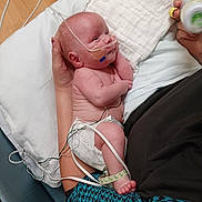 Damon is registered to the contest to win money with this photo: baby, infant, hospital, medical_tubes, diaper, adult_hand, bottle, bed, blanket, sensor_wires, patient, care, healthcare, newborn, person, medical_care, lying_down, hospital_room, cute, tender_moment
