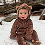 baby, child, snow, forest, brown_onesie, hood, cute, drool, sitting, winter_clothing, outdoor, nature, logs, pine_needles, eyes, face, warm_clothes, fur_texture, footwear, hood_ears