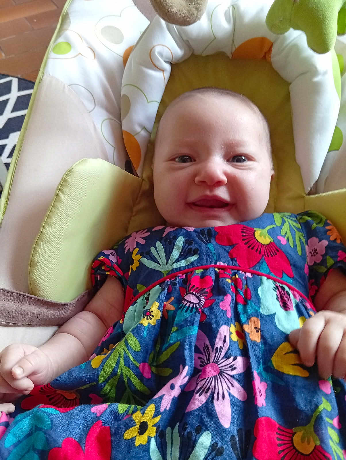 Eléna participe au concours pour gagner de l'argent avec cette photo : baby, child, smiling, floral_dress, colorful_clothing, infant, cushion, baby_seat, indoor, happy, person, face, skin, head, arm, hand, fabric, pattern, comfort, cute