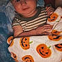 Jasper is registered to the contest to win money with this photo: baby, child, blanket, pumpkin, striped_clothing, smile, bed, cozy, hands, face, infant, pajamas, cute, comfort, soft_light, indoor, person, resting, young, wrapped