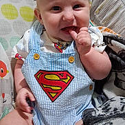 Jasper joined the competition — help win amazing prizes! baby, child, superman_logo, overalls, blanket, smiling, indoors, cute, infant, seated, furniture, patterned, clothing, happy, face, hand, skin, head, person, comfort