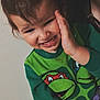toddler, child, person, face, smile, hand, clothing, sweater, cartoon_characters, teenage_mutant_ninja_turtles, hair, indoor, wall, expression, playful, closeup, adult, partial_face, skin, portrait