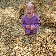 Mya participe au concours pour gagner de l'argent avec cette photo : child, girl, purple_clothing, straw, hay, outdoor, field, sunlight, nature, standing, person, smile, expression, grass, daytime, casual, cute, young, portrait, playful