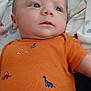 baby, infant, onesie, orange_clothing, dinosaur_print, blue_eyes, blanket, soft_fabric, lying_down, child, cute, portrait, casual, indoor, young_child, face, skin, head, expression, clothing