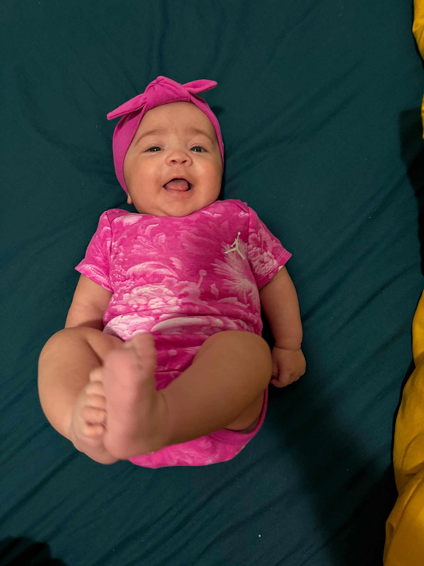 Keïssy a rejoint le concours — aidez-le/la à gagner de superbes lots ! baby, infant, pink_clothing, headband, smiling, happy, barefoot, lying_down, cute, child, human, skin, feet, tongue_out, indoors, fabric, textile, playful, portrait, person