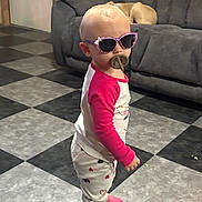 Oaklynn is registered to the contest to win money with this photo: toddler, child, sunglasses, pacifier, indoor, floor, checkered_floor, pajamas, pink_sleeves, standing, dog, couch, gray_couch, hair, light_hair, person, footwear, sock, cute, home