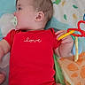 baby, infant, child, lying_down, pacifier, red_onesie, toy, play_mat, colorful, portrait, side_profile, sleepy, indoor, nursery, baby_clothing, hand, face, hair, patterned_blanket, safe