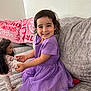 child, girl, smile, purple_dress, doll, toy, couch, indoor, happy, playing, pajamas, furniture, home, cute, portrait, young_child, long_hair, holding_hands, seated, relaxed