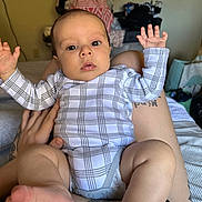 Jensen is registered to the contest to win money with this photo: baby, infant, person, clothing, onesie, tattoo, hand, foot, face, indoor, bed, blanket, adult, skin, legs, expression, looking, casual, comfort, home