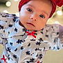 apparel, baby, bokeh, child, closeup, cute, expression, eyes, face, fashion, headband, holiday_theme, indoors, infant, portrait, red_bow, snowflake_pattern, soft_lighting, white_outfit, young