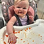 baby, high_chair, food, messy, kitchen, child, smiling, face, hand, cushion, purple_clothing, feeding, orange_food, tray, indoor, person, happy, hair, seatbelt, table