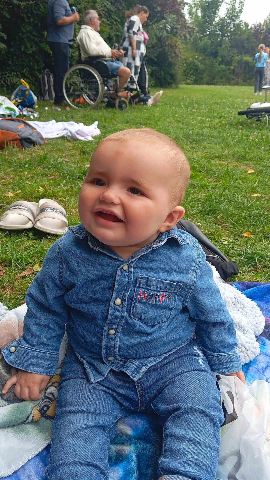 Kenny a rejoint le concours — aidez-le/la à gagner de superbes lots ! baby, denim_clothing, outdoor, grass, blanket, happy, child, person, wheelchair, adult, casual_clothing, greenery, park, smile, sitting, footwear, nature, daylight, family, relaxation