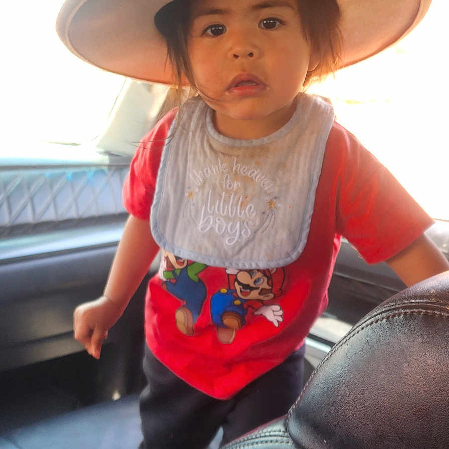 Jjr is registered to the contest to win money with this photo: bib, car_interior, casual_clothing, child, curious_expression, face, hat, indoors, leather_seat, person, portrait, red_shirt, seat, standing, super_mario, toddler, vehicle, window, young_boy, young_child