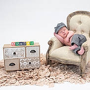 Arthur is registered to the contest to win money with this photo: baby, newborn, sleeping, armchair, vintage_furniture, checkered_clothing, cap, pants, decorative_blocks, name_blocks, drawer_chest, rug, beige, white_background, cozy, portrait, infant, peaceful, studio_photo, soft_lighting