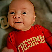 Hawlstin is registered to the contest to win money with this photo: baby, infant, red_shirt, freshman, face, smile, person, young_child, portrait, cute, indoors, clothing, sleeve, expression, head, skin, eyes, mouth, hand, background