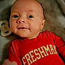 baby, infant, red_shirt, freshman, face, smile, person, young_child, portrait, cute, indoors, clothing, sleeve, expression, head, skin, eyes, mouth, hand, background