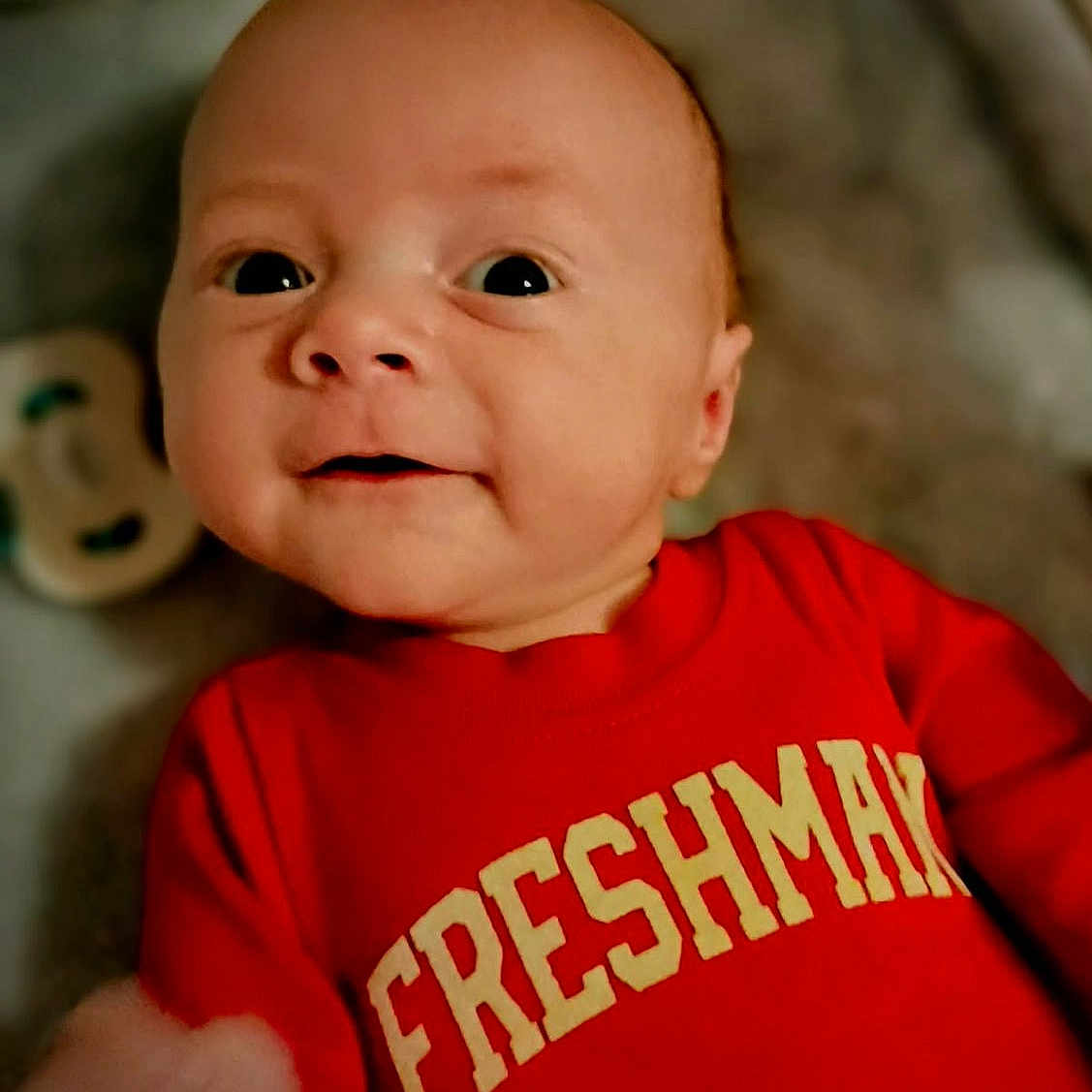 Hawlstin is registered to the contest to win money with this photo: baby, infant, red_shirt, freshman, face, smile, person, young_child, portrait, cute, indoors, clothing, sleeve, expression, head, skin, eyes, mouth, hand, background