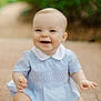 baby, child, smiling, sitting, blue_dress, white_collar, outdoor, nature, happy, face, skin, hands, legs, pavement, background_blur, cute, young, portrait, infant, bright