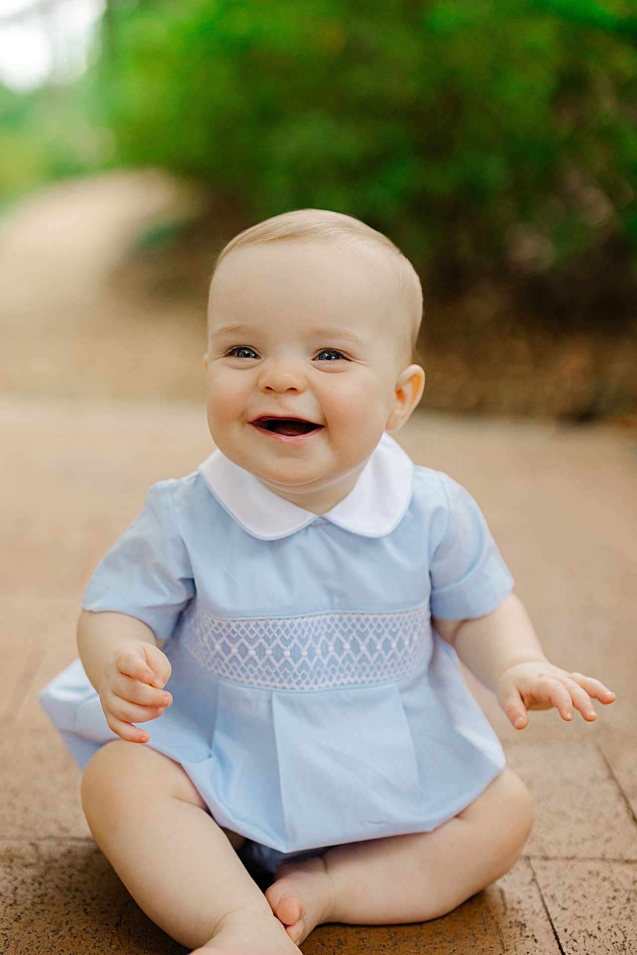 Liam is registered to the contest to win money with this photo: baby, child, smiling, sitting, blue_dress, white_collar, outdoor, nature, happy, face, skin, hands, legs, pavement, background_blur, cute, young, portrait, infant, bright