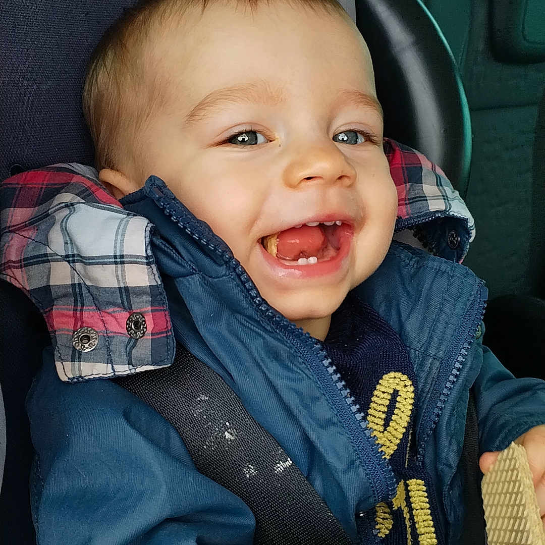 Elyass a rejoint le concours — aidez-le/la à gagner de superbes lots ! toddler, child, smiling, happy, car_seat, seatbelt, blue_jacket, snack, wafer, indoor, portrait, cute, baby, clothing, hands, face, head, car_interior, window, seat