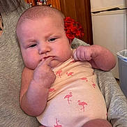 Chayanna is registered to the contest to win money with this photo: adult, baby, cabinet, cute, expression, face, flamingo, flower, hand, holding, indoor, infant, kitchen, onesie, person, pink, portrait, refrigerator, skin, tattoo