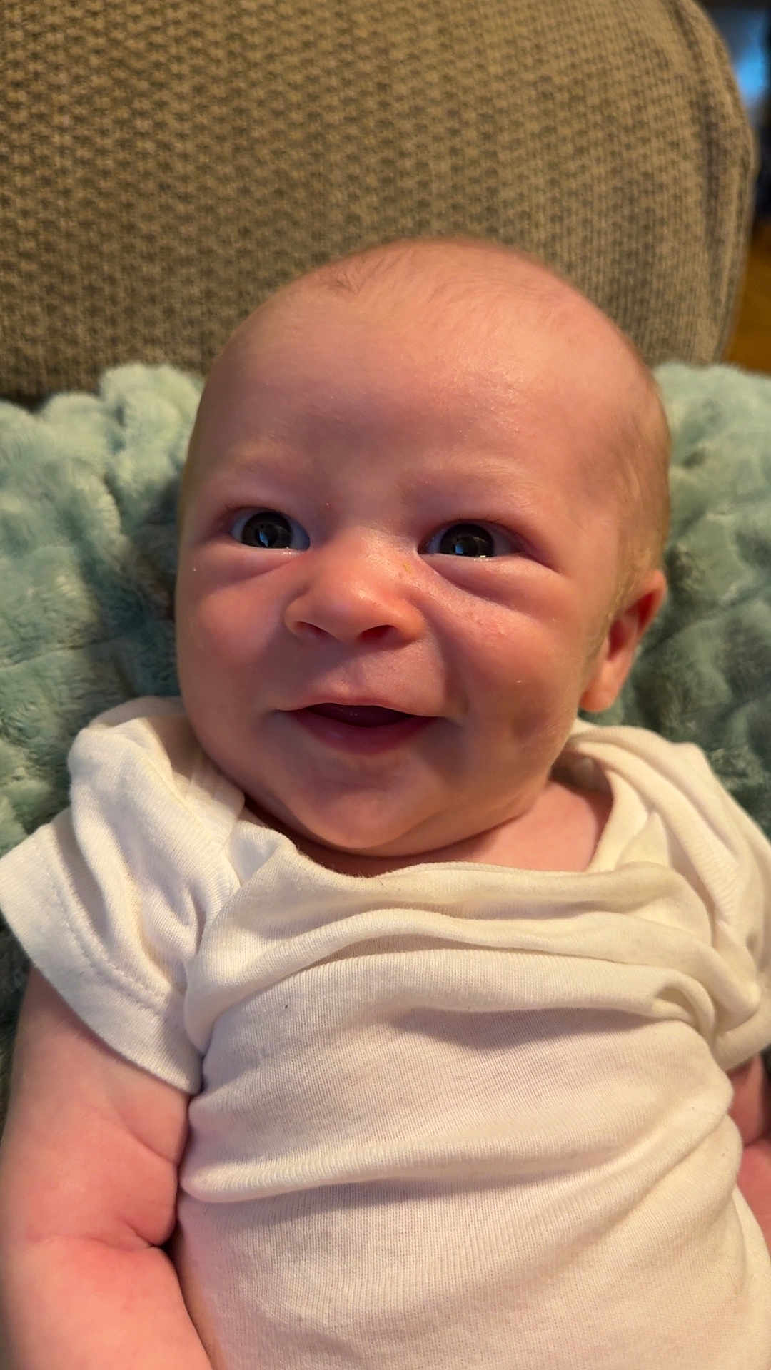 Colton is registered to the contest to win money with this photo: baby, infant, smile, white_onesie, soft_blanket, cushion, face, skin, person, cute, newborn, happy, indoors, child, head, eyes, mouth, arm, expression, portrait