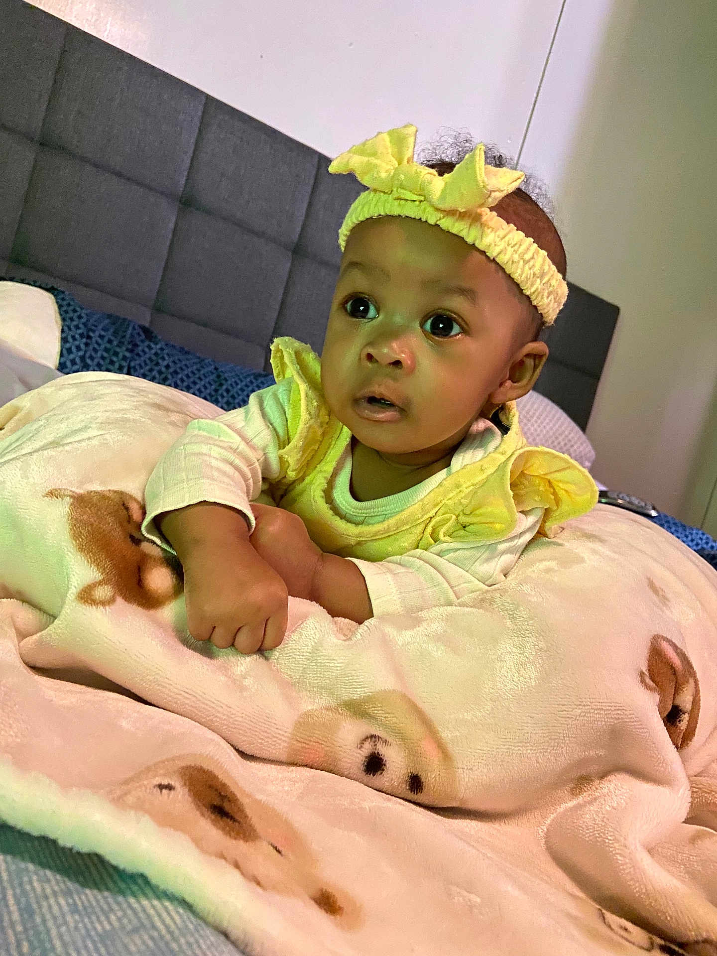 Avalynn is registered to the contest to win money with this photo: baby, child, blanket, headband, yellow_clothing, bed, pillow, face, infant, curious, indoors, soft_texture, animal_print, cute, portrait, resting, young_child, cozy, sleep_area, warm
