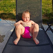 Agathe a rejoint le concours — aidez-le/la à gagner de superbes lots ! toddler, child, outdoor, sunlight, lawn_chair, pink_swim_diaper, grass, fence, summer, relaxing, barefoot, baby, mesh_chair, sunny_day, young_child, sitting, backyard, nature, casual, daytime